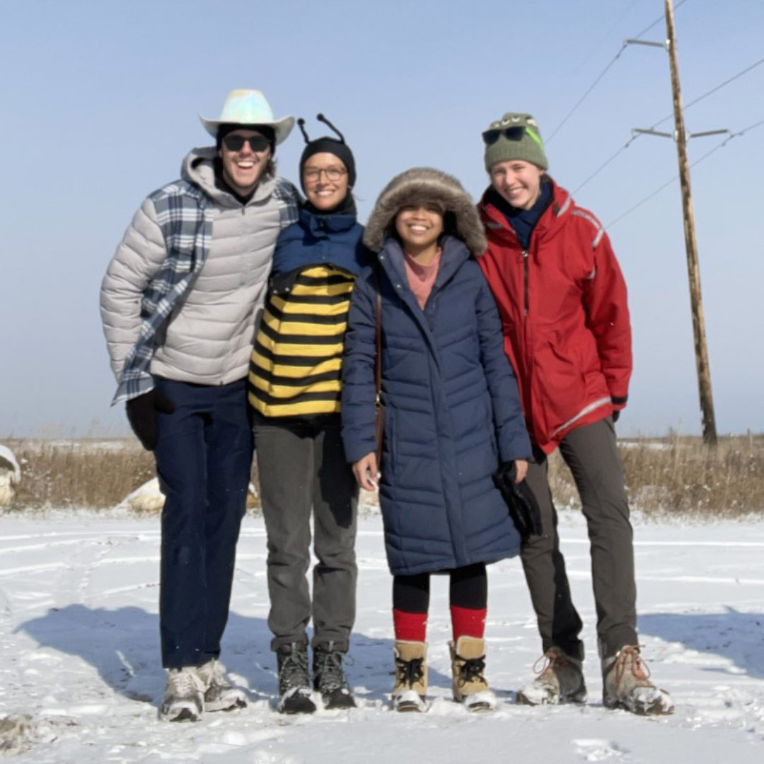 Four people smiling while standing in the snow